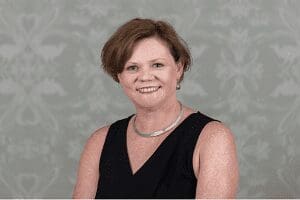Middle-aged woman with short brown hair smiling, wearing black sleeveless top and necklace.