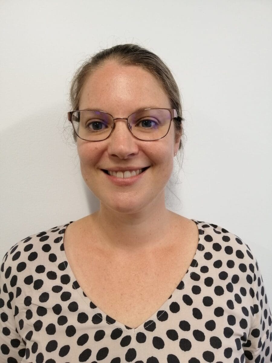Woman with brown hair in glasses smiling, wearing a light top with black polka dots, white background