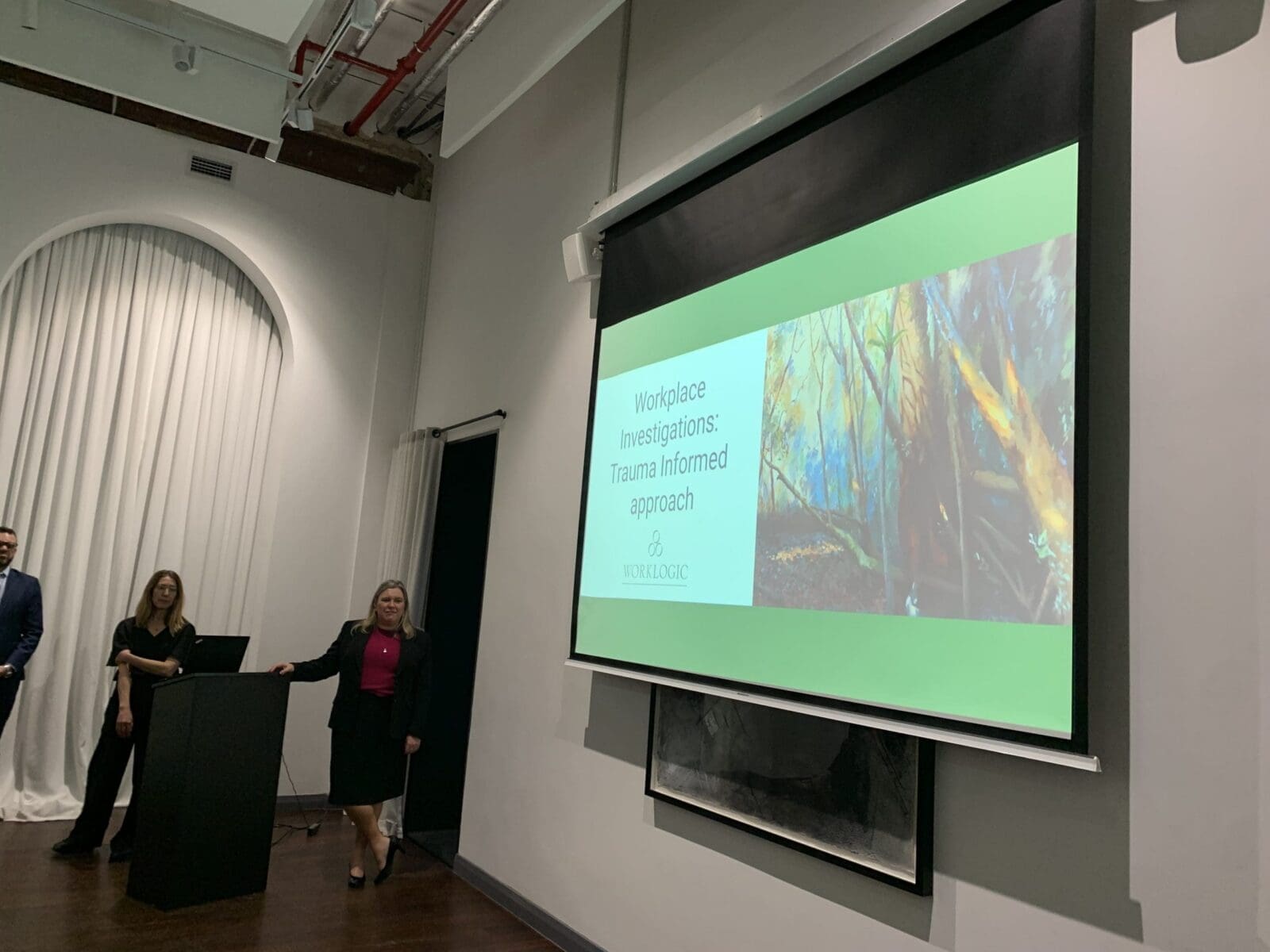 Workplace Investigations Trauma Informed approach presentation displayed on a screen in a room.