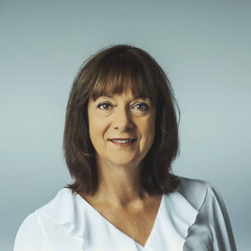 Middle-aged woman with brown hair wearing a white blouse against a plain light grey background