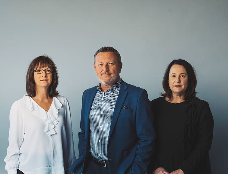 Three adults standing side by side against a plain grey background