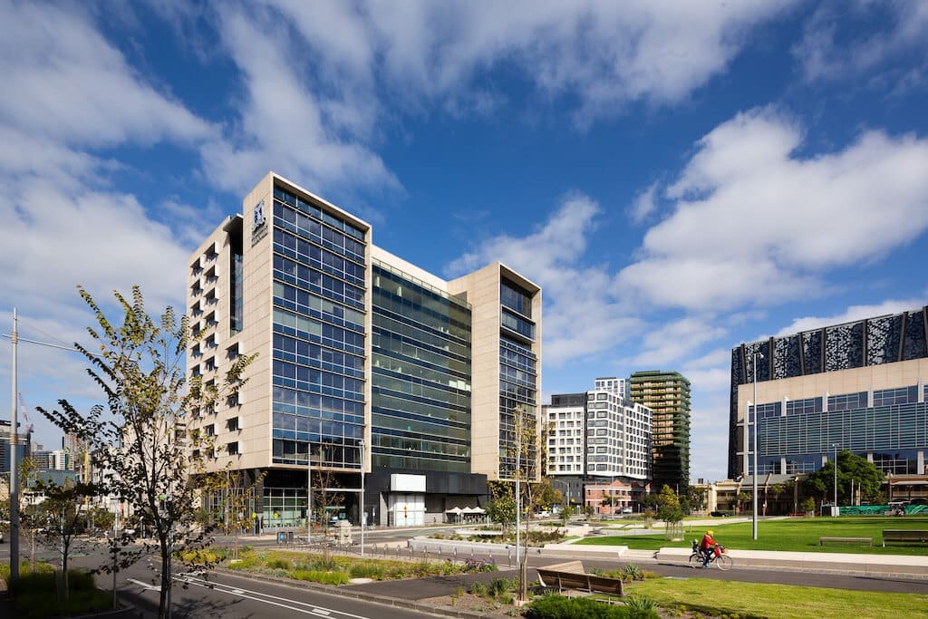 Mid-rise office and residential buildings around landscaped lawns with benches under a blue sky.