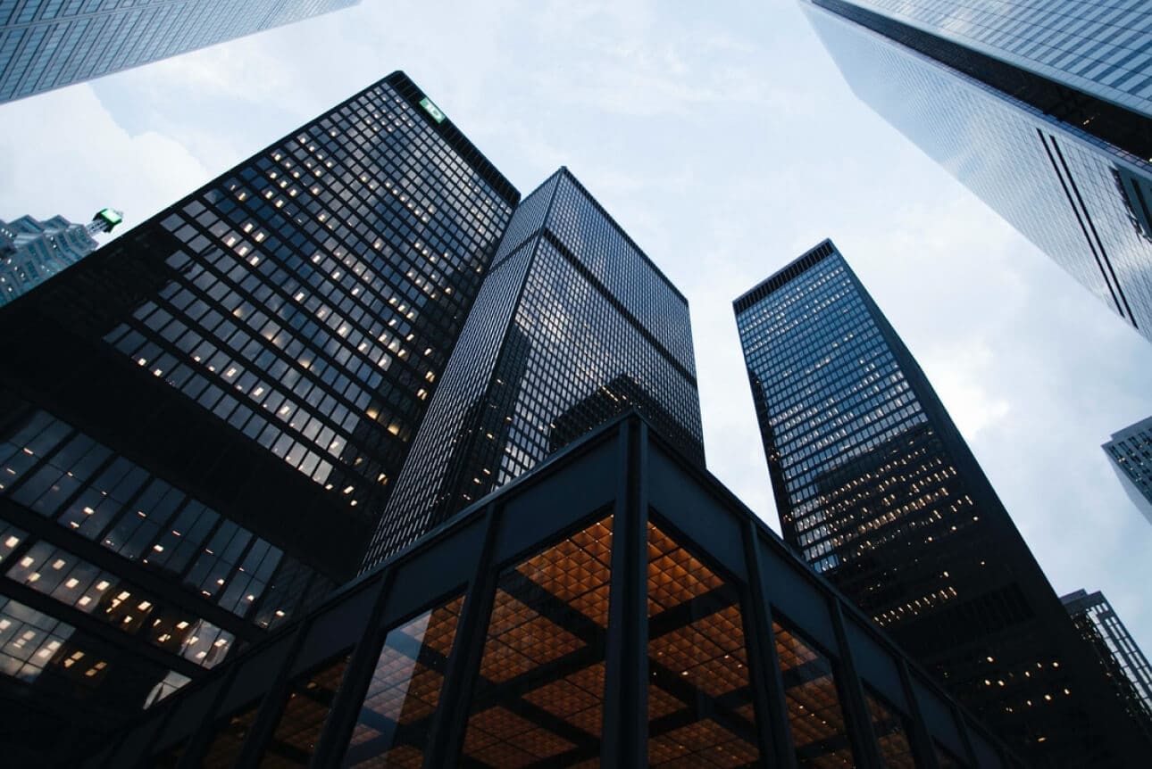 Tall office buildings with illuminated windows viewed from below under a cloudy sky.