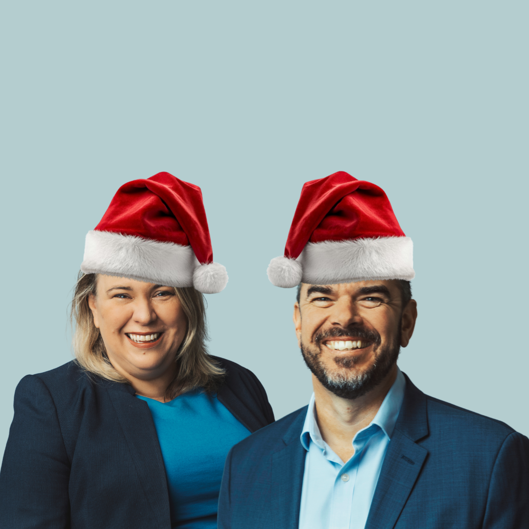 Man and woman in business attire wearing red and white Santa hats on a light blue background